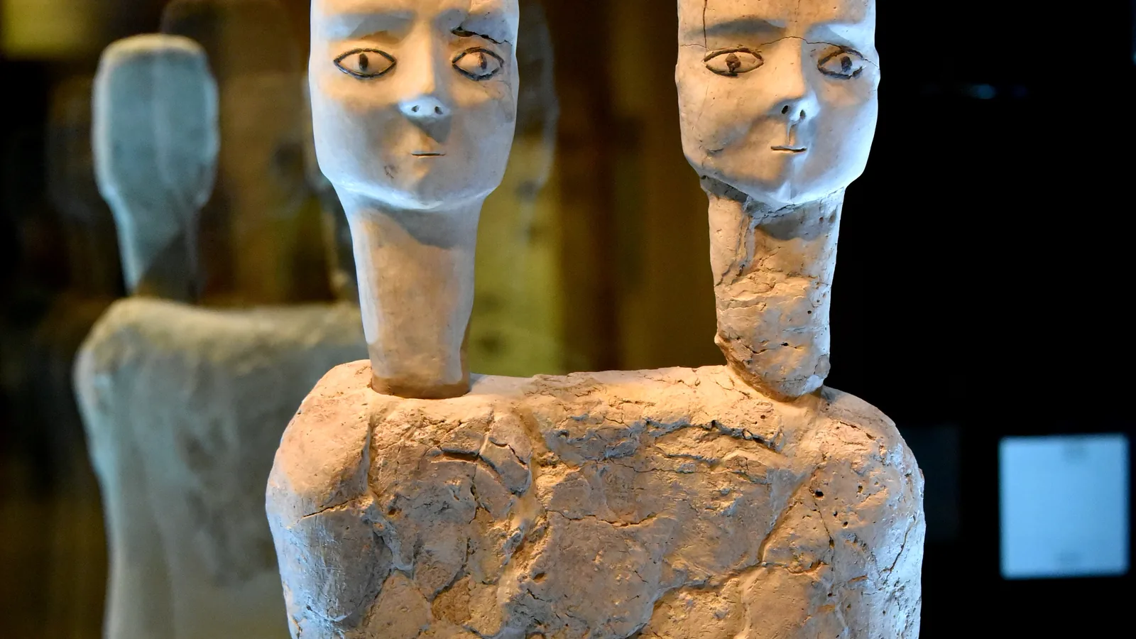 Two-headed lime-plaster bust with painted eyes, damaged surface, museum display case
