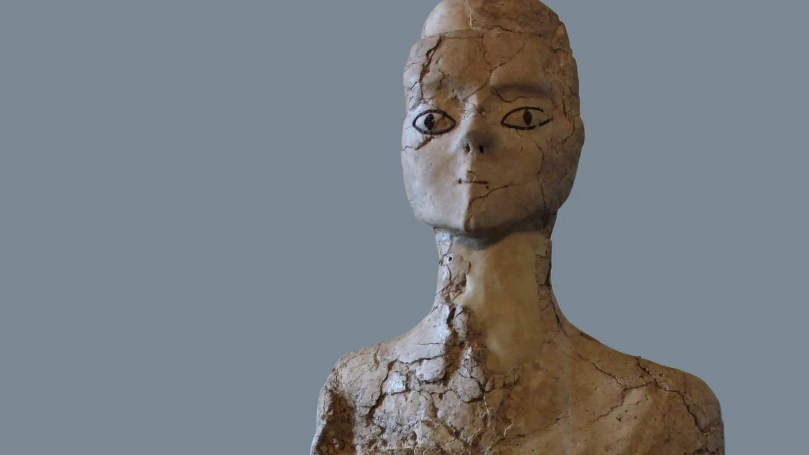 Standing lime-plaster human statue with painted eyes and cracked surface, plain background