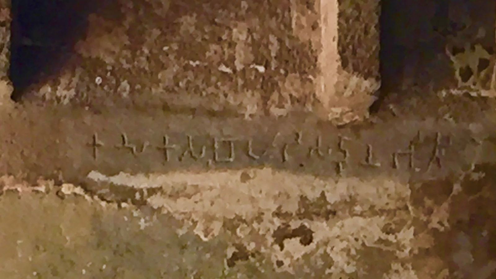 A line of ancient Brahmi letters cut into weathered rock beside a carved arch