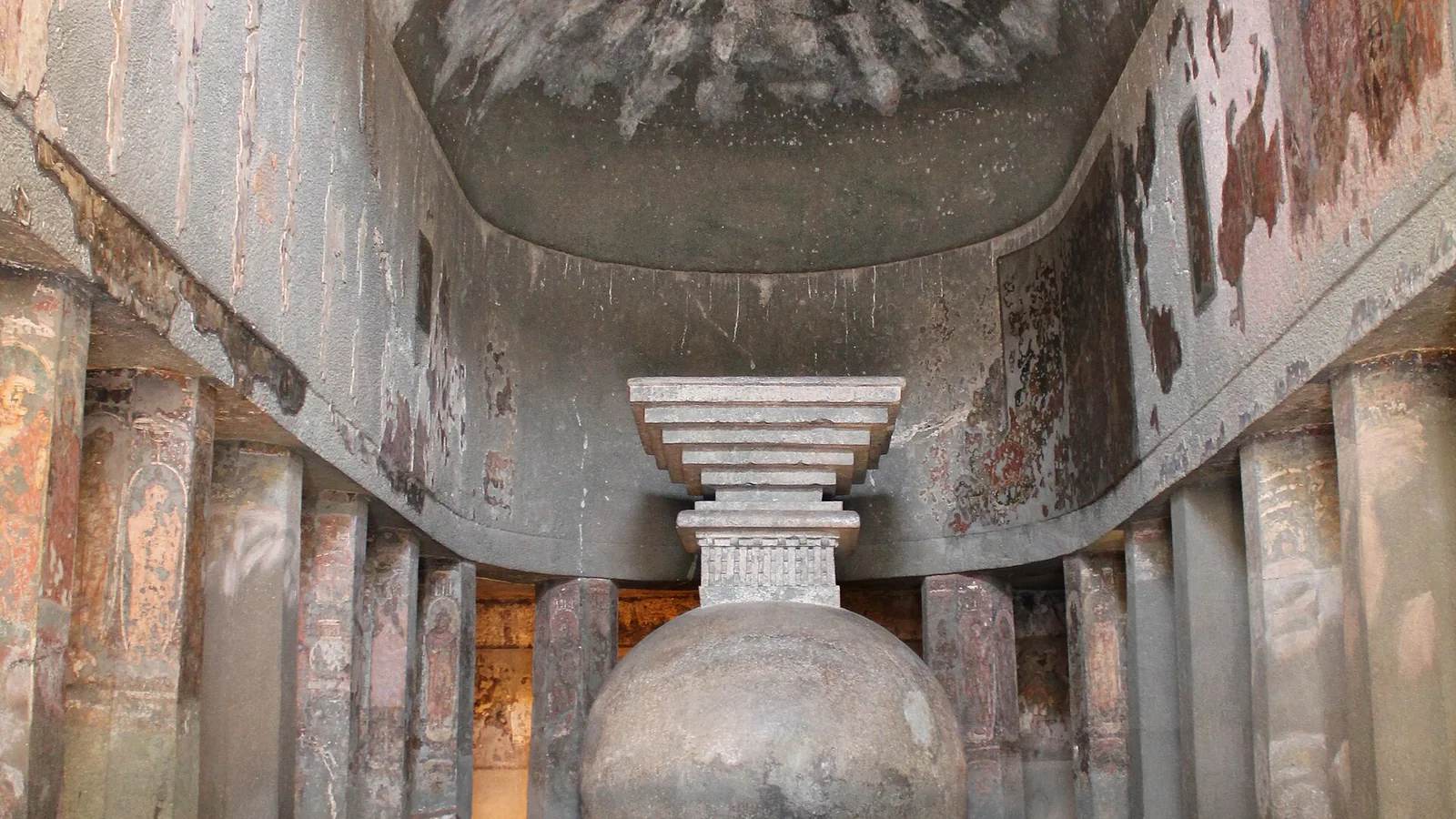 a rock-cut vaulted hall with rows of octagonal pillars leading to a plain stone stupa at the far end