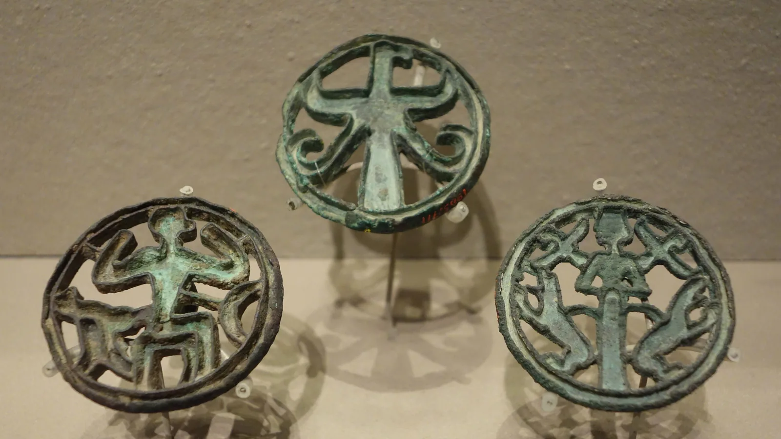 three round openwork bronze seals with animal and human figures, mounted in a museum case