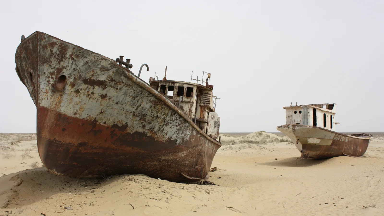Rusting fishing ships stranded on dry sandy ground under a wide sky