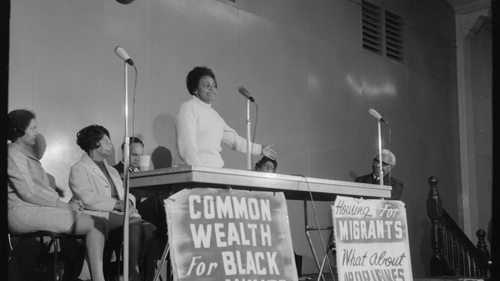 Black and white photograph of Faith Bandler speaking at a table with other FCAATSI members in a hall