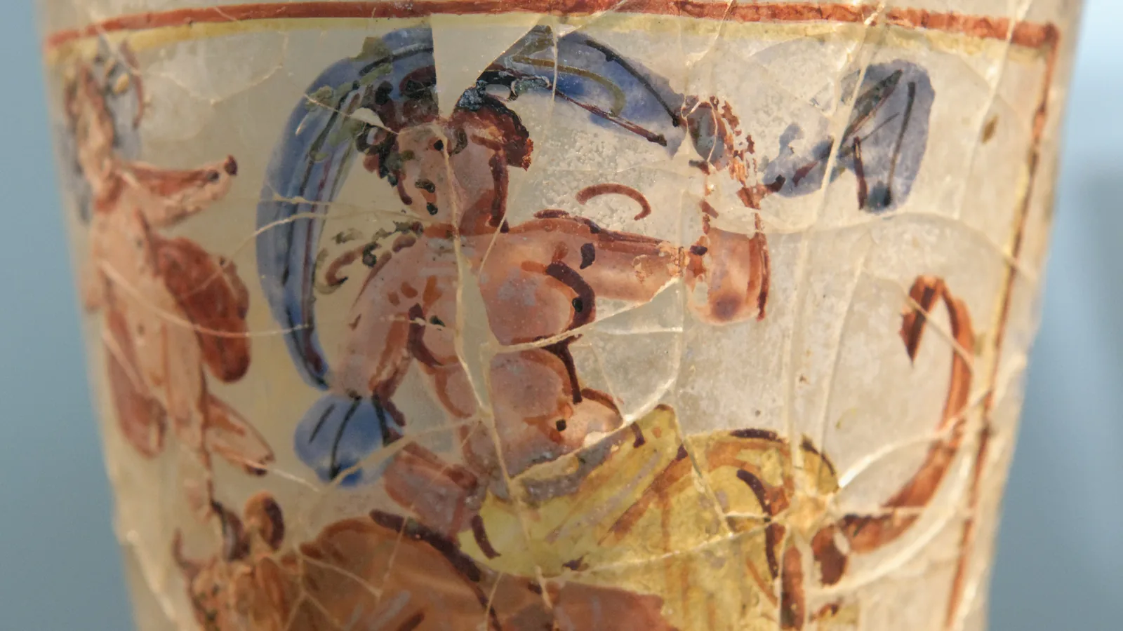 a painted glass goblet with figures in red, blue and yellow on a pale ground, showing a woman carried on a bull