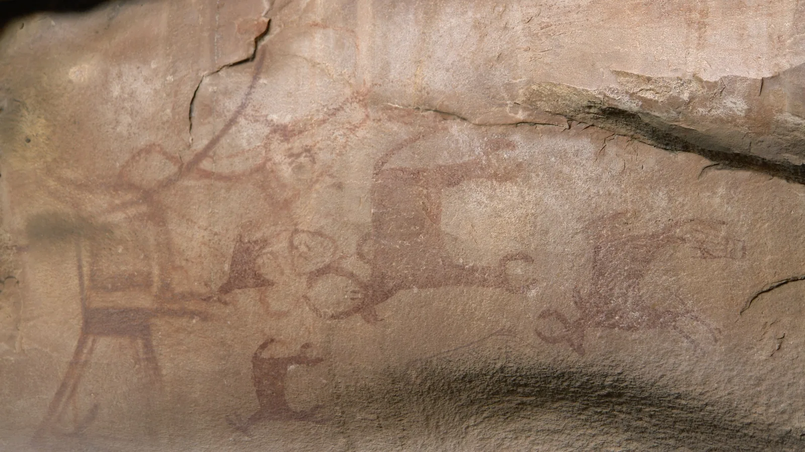 red and white figures of animals and people painted on a rock shelter wall