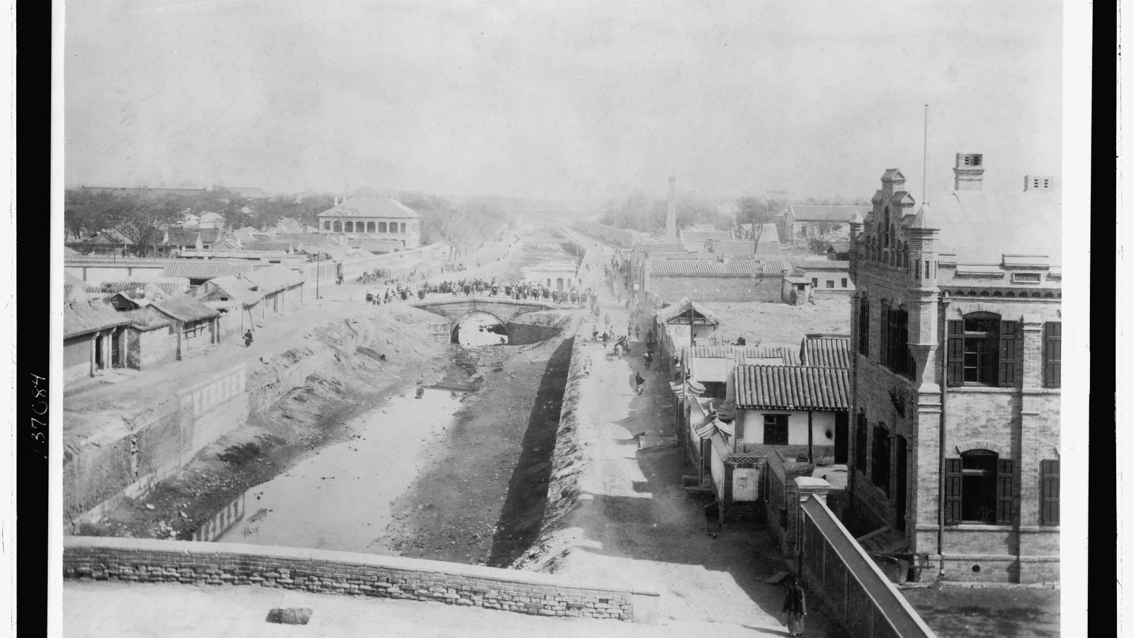 Street view of the walled Peking legation quarter with flags, 1900