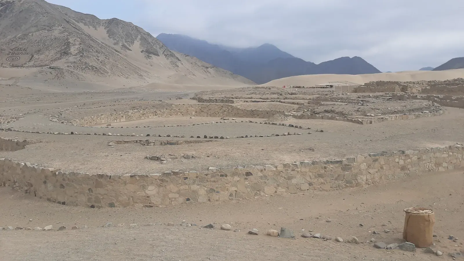 low stone walls and a sunken circular plaza on a dry valley floor with mountains behind