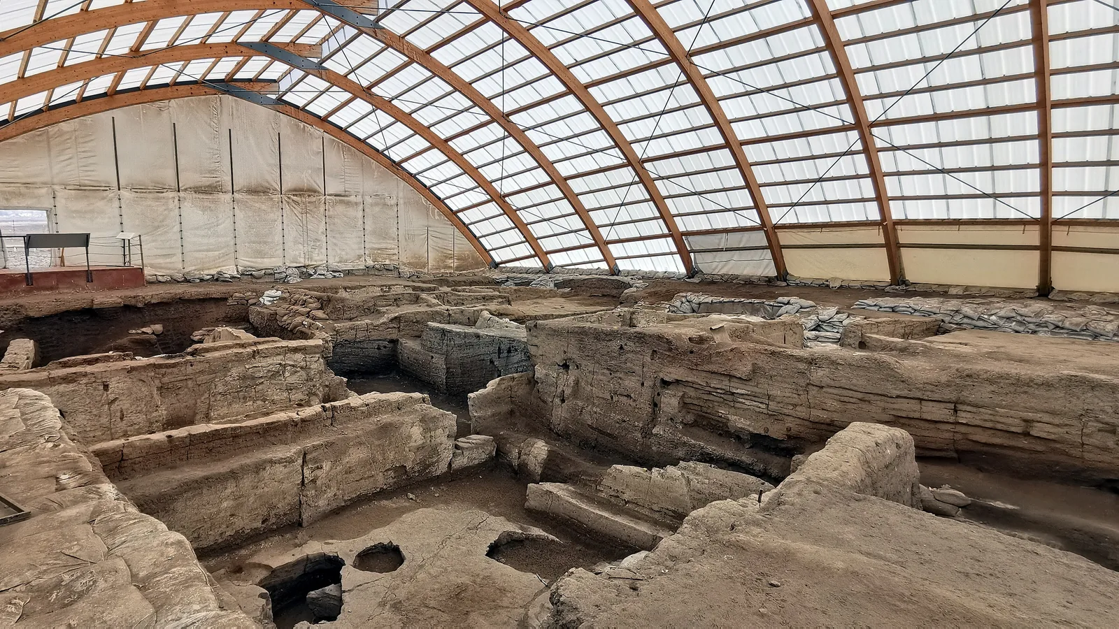excavated mud-brick house walls packed side by side under a large timber-and-fabric shelter