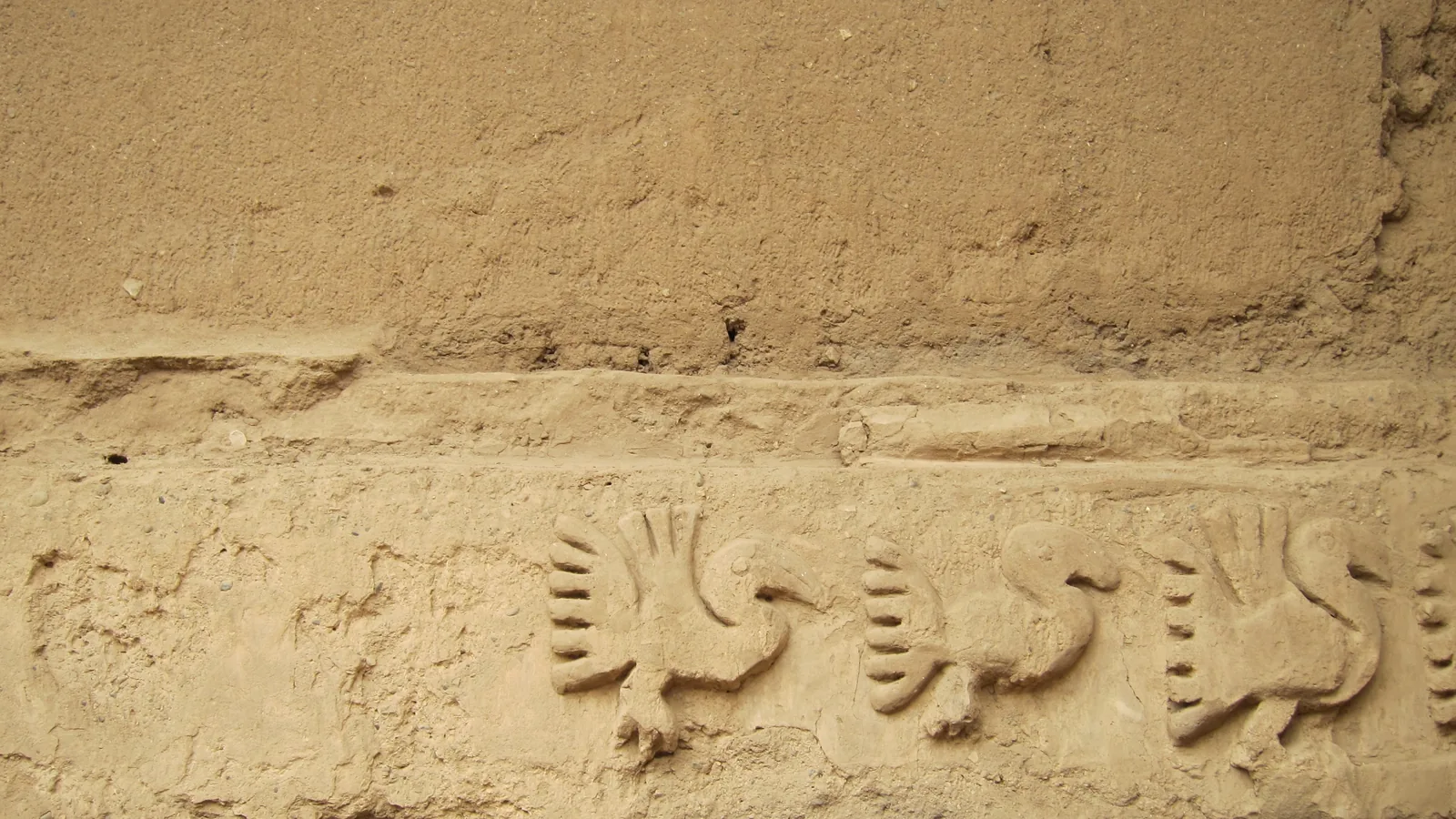 Adobe wall relief showing a repeated pelican motif in raised carved plaster
