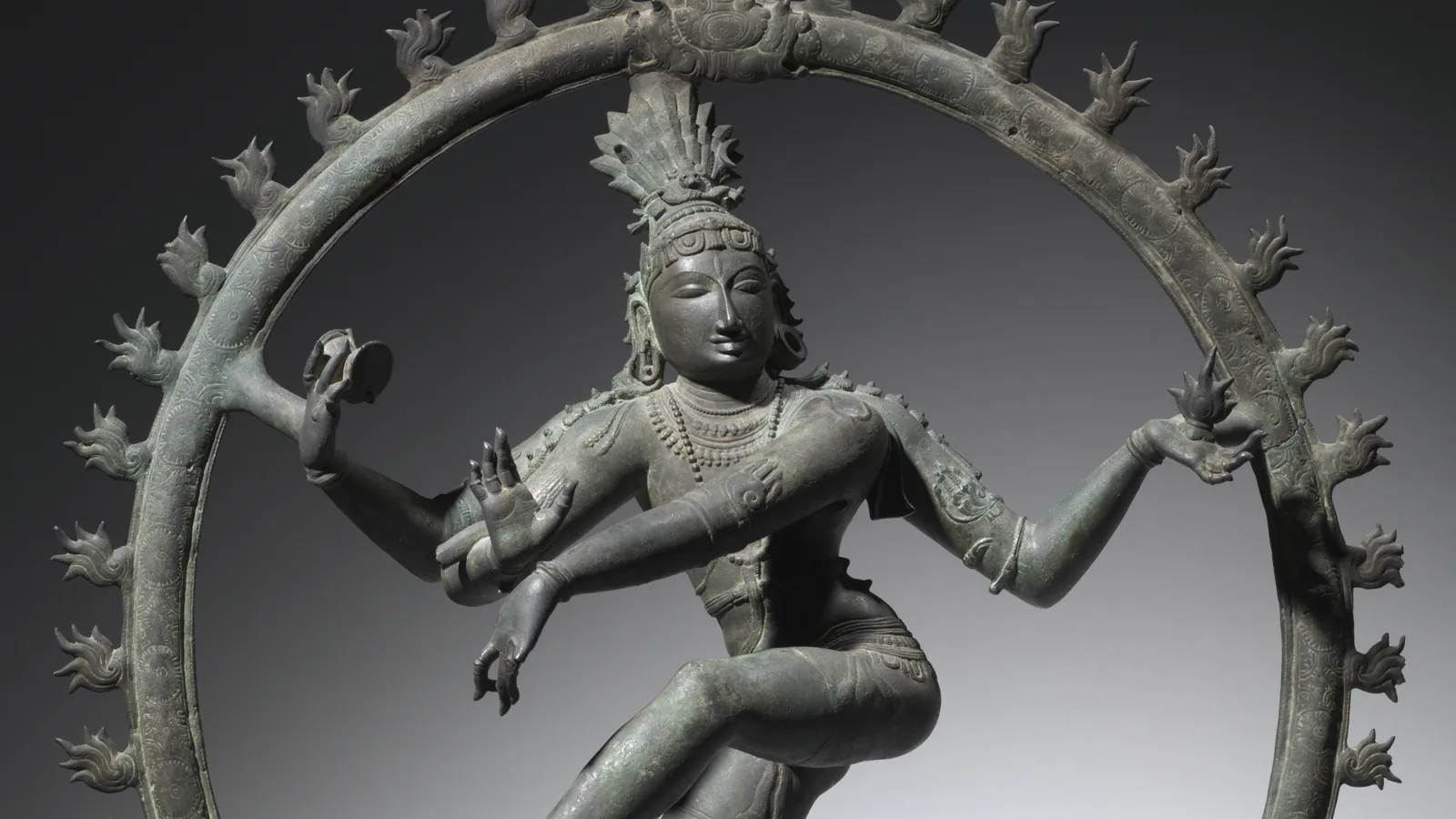 a bronze figure of a four-armed dancing deity within a ring of flames, one foot raised