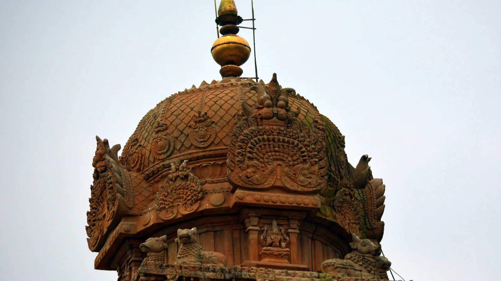 the upper storeys of a pyramidal stone temple tower with carved niches and a domed cap against the sky