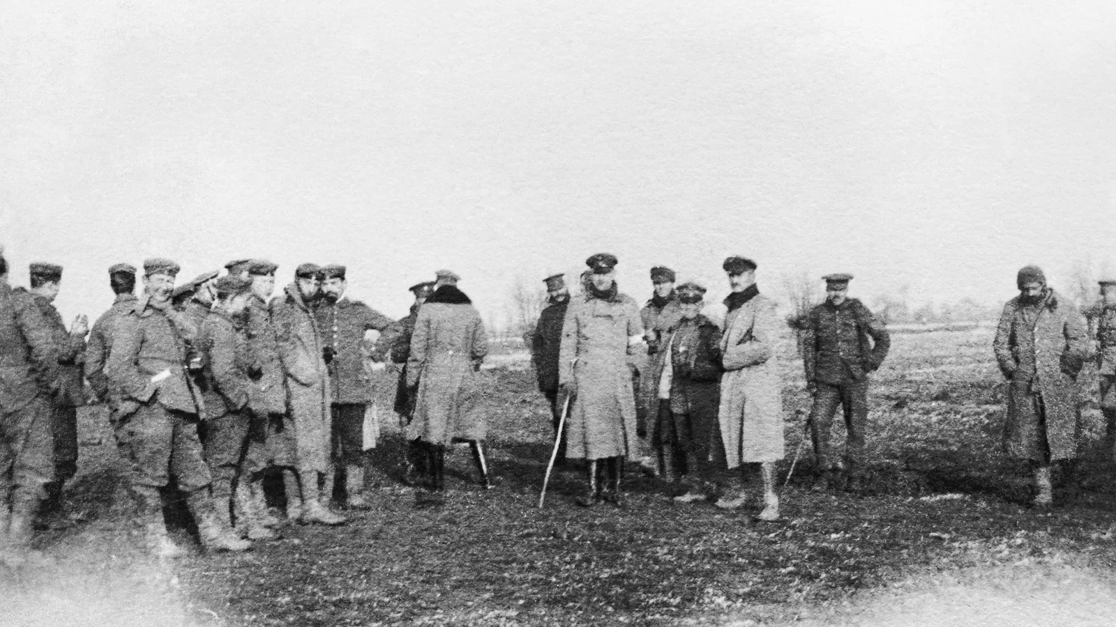 British and German soldiers in greatcoats standing together in a muddy field between the trenches