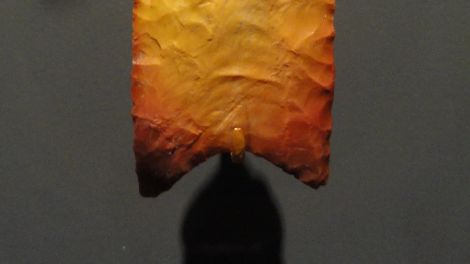 the lower half of a chipped orange chert spear point showing the flute channel at its base, on a gray background