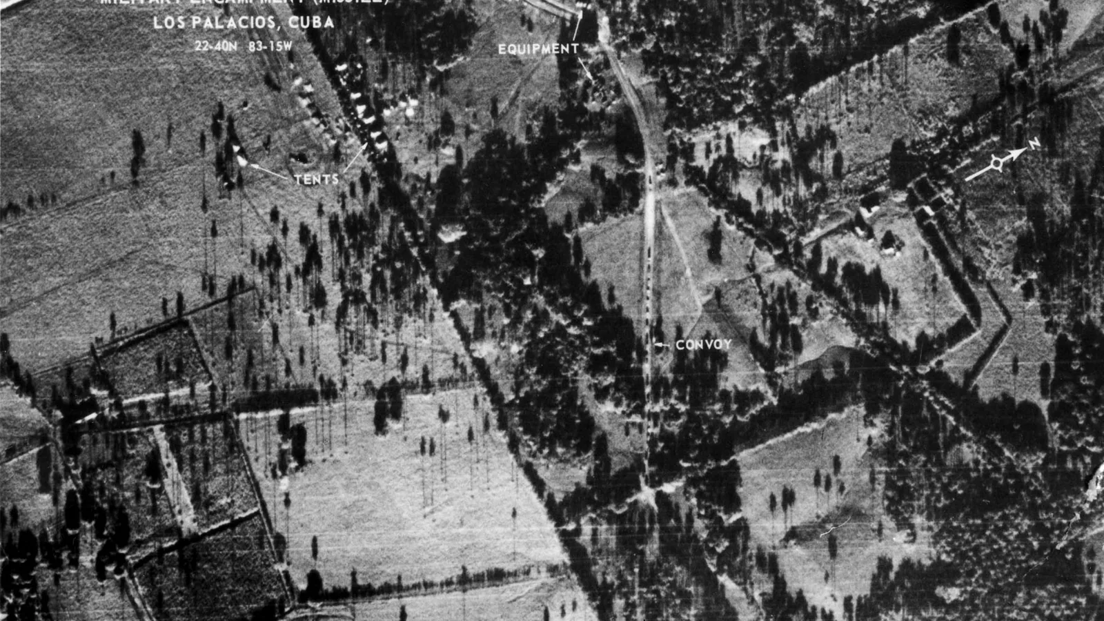 an aerial reconnaissance photograph of a wooded site with roads, tents and vehicles marked with typed labels