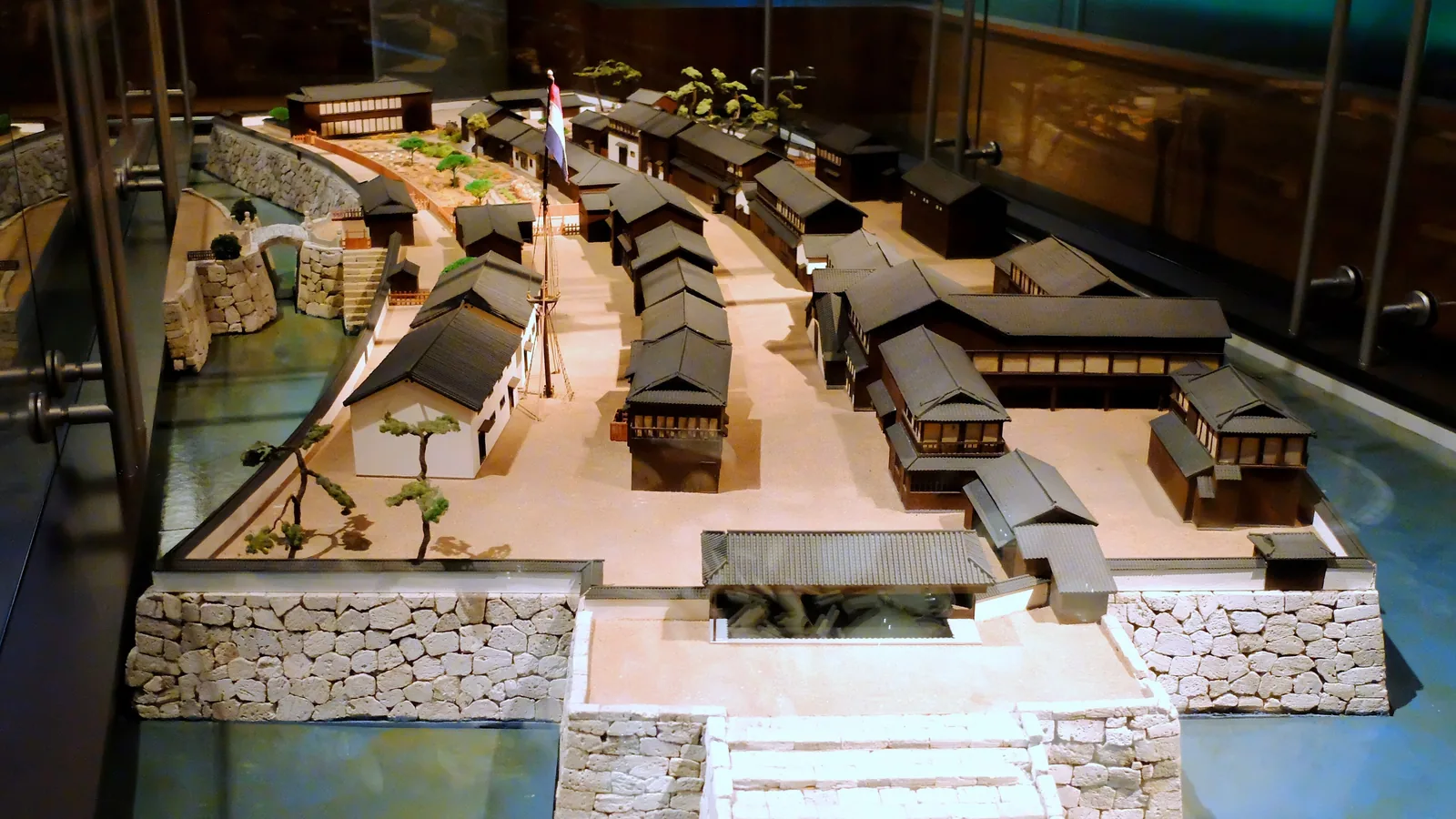 Scale model of a small fan-shaped island packed with tiled houses along a single street, joined to the shore by a bridge
