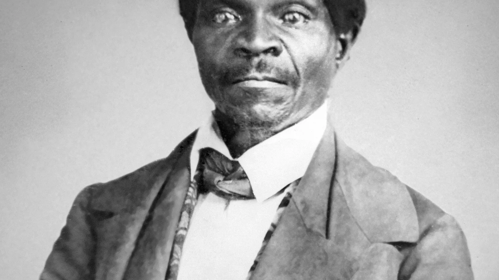 Seated studio photograph of Dred Scott in a dark coat, hands folded