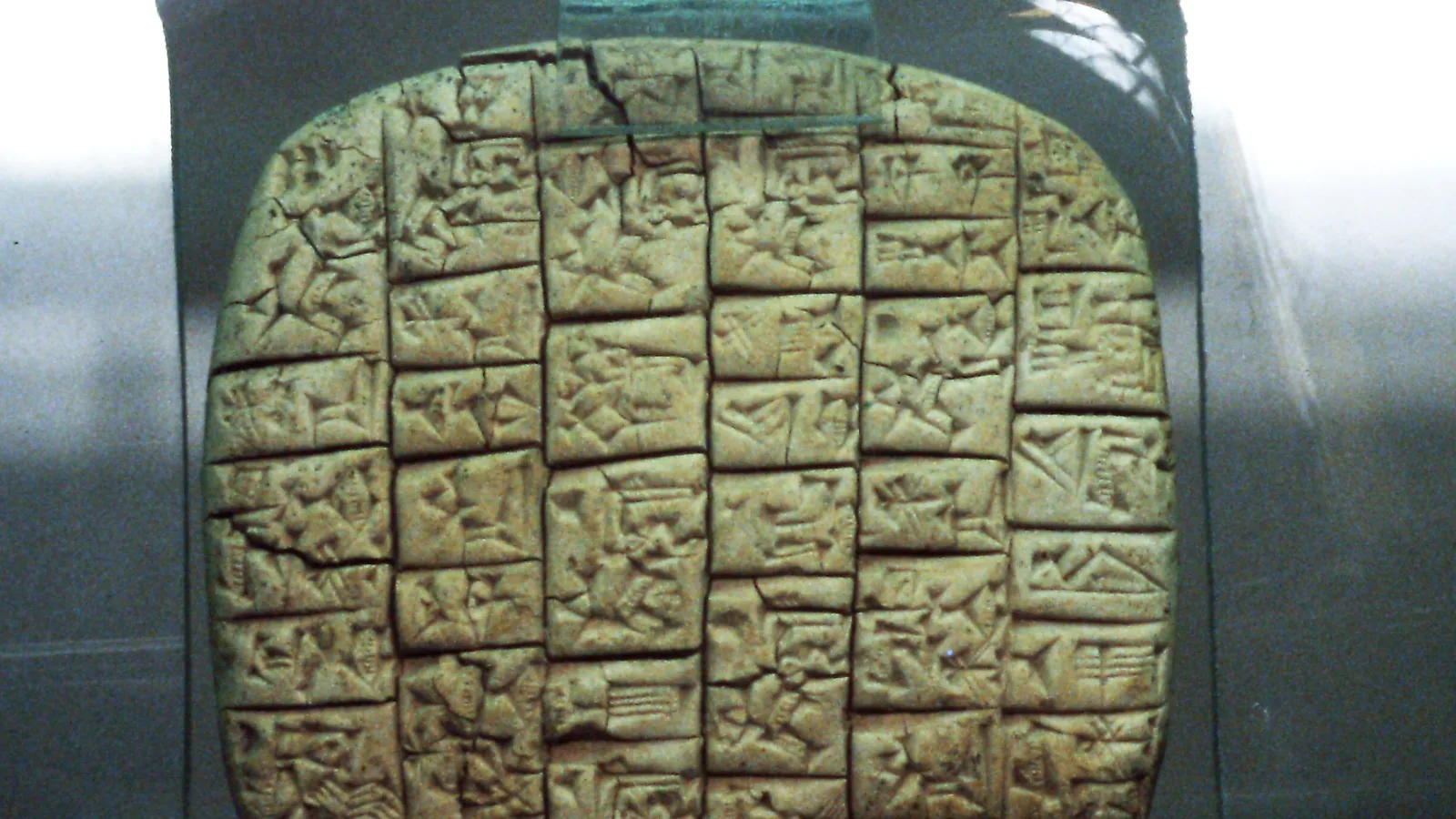 Square cuneiform clay tablet with rows of wedge-shaped script, in a museum display case