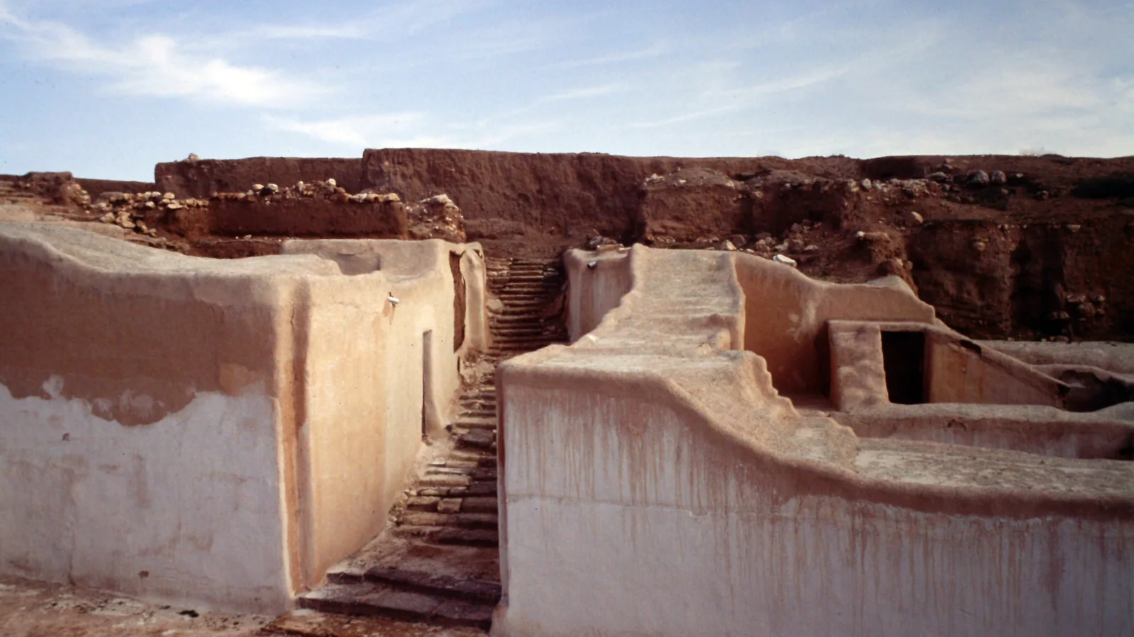 Excavated mudbrick walls and a stone stairway at an archaeological mound