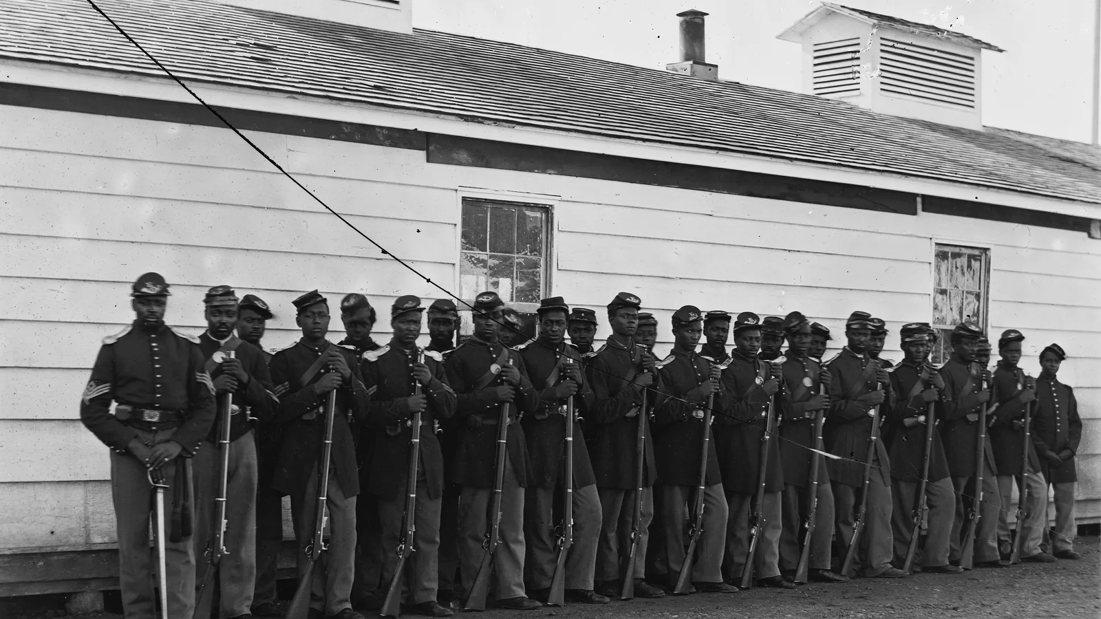 a company of Black Union soldiers in uniform standing in formation outdoors