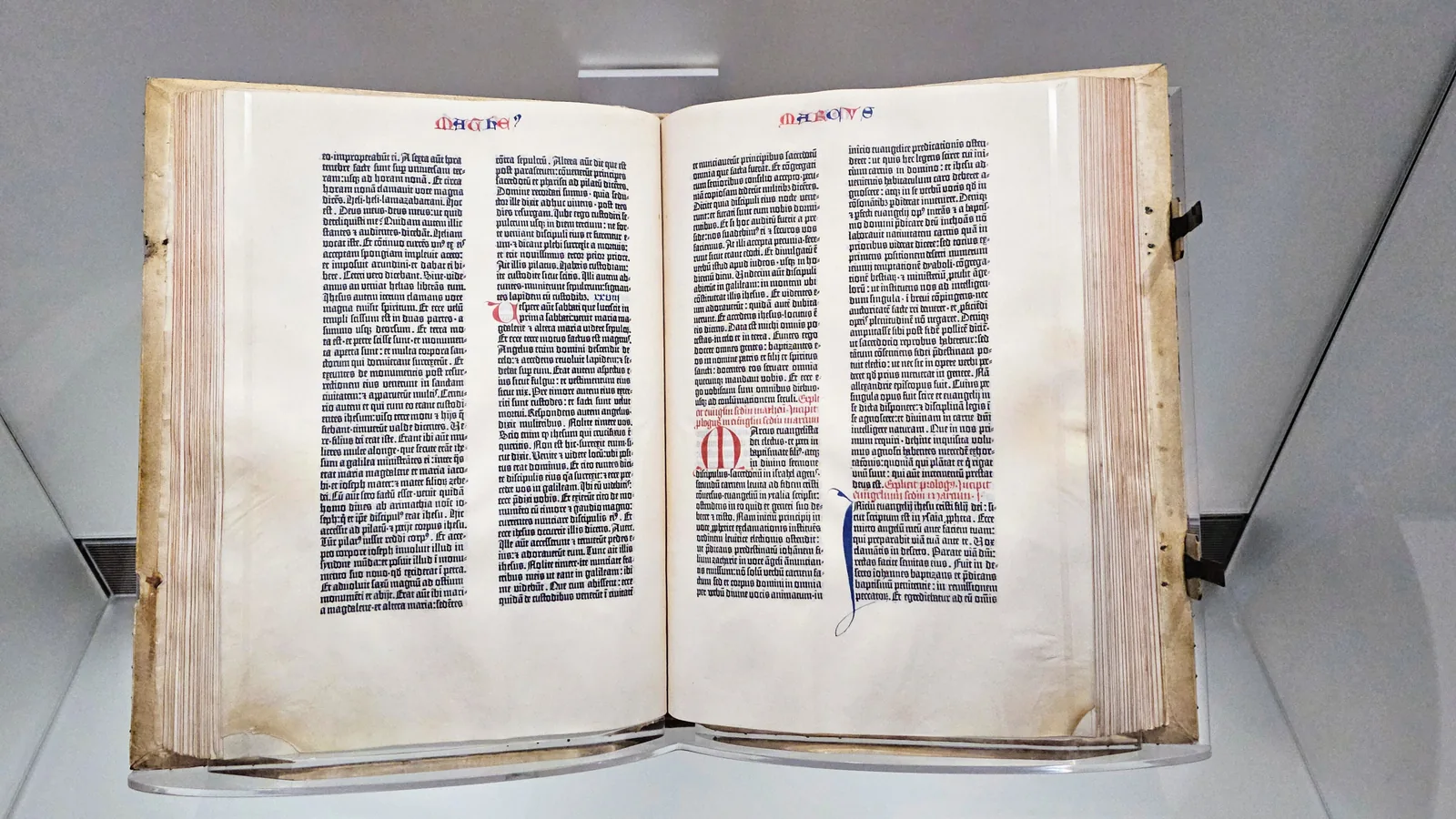 an open printed book with two columns of dense black gothic type and colored initials on each page