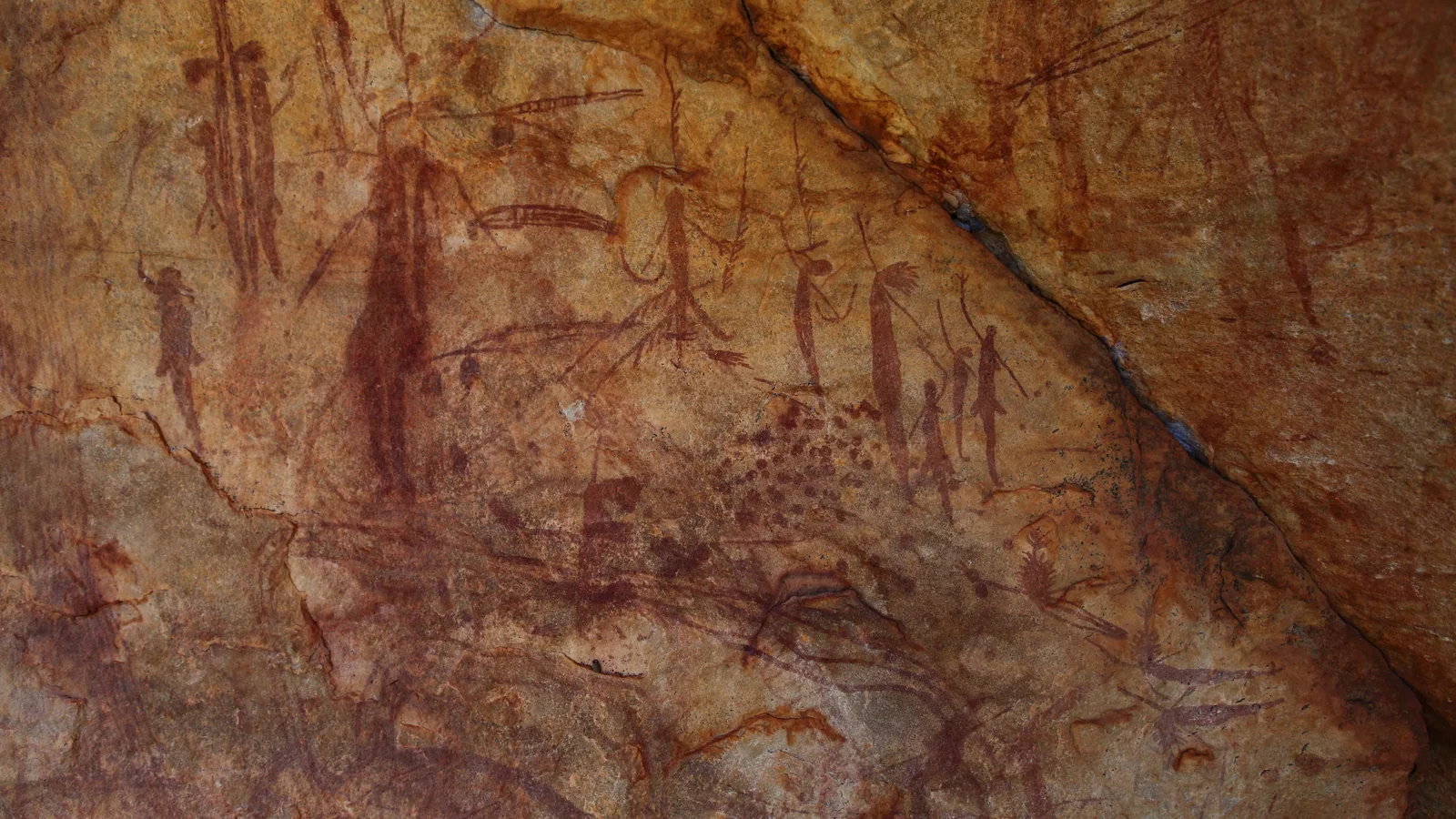 slender dark-red painted human figures with tassels, on the orange-brown rock of a shelter wall