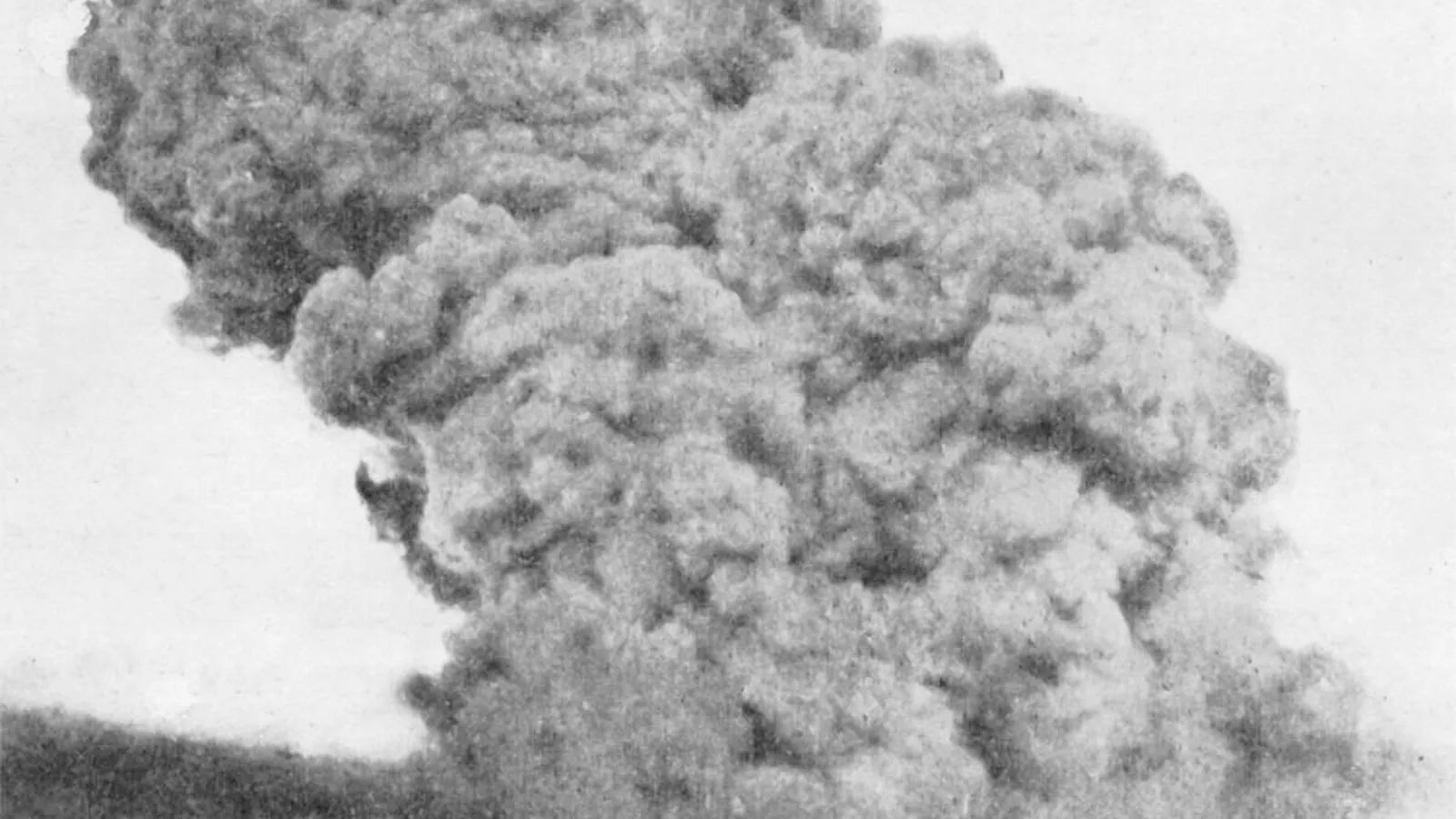 Tall vertical cloud rising over a harbor, seen from a distance