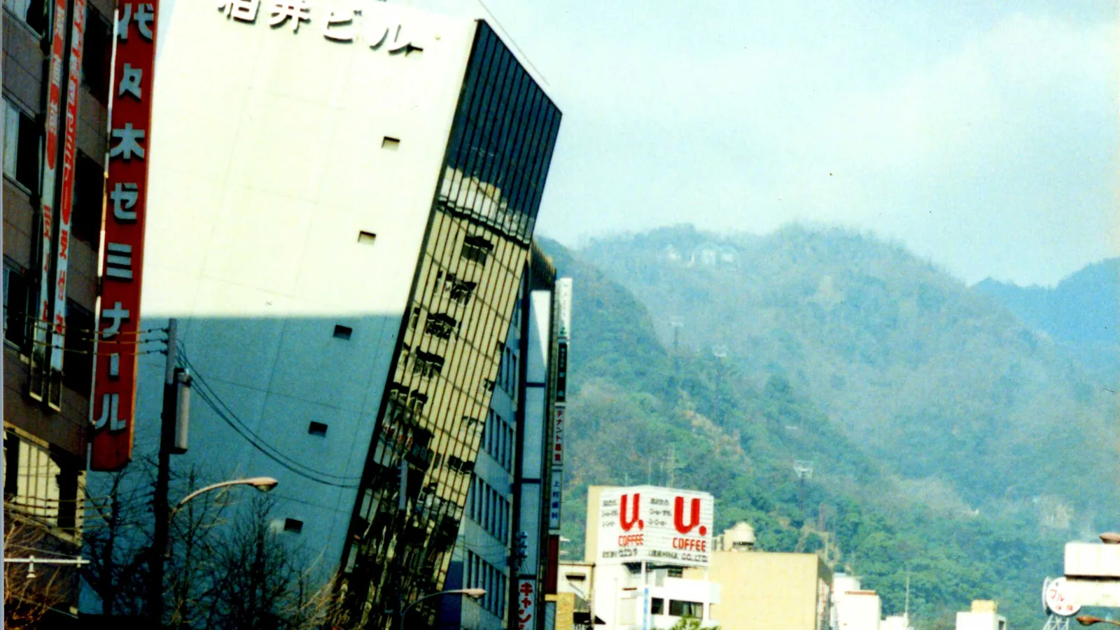 A multi-story building caught in the moment of collapsing onto a street