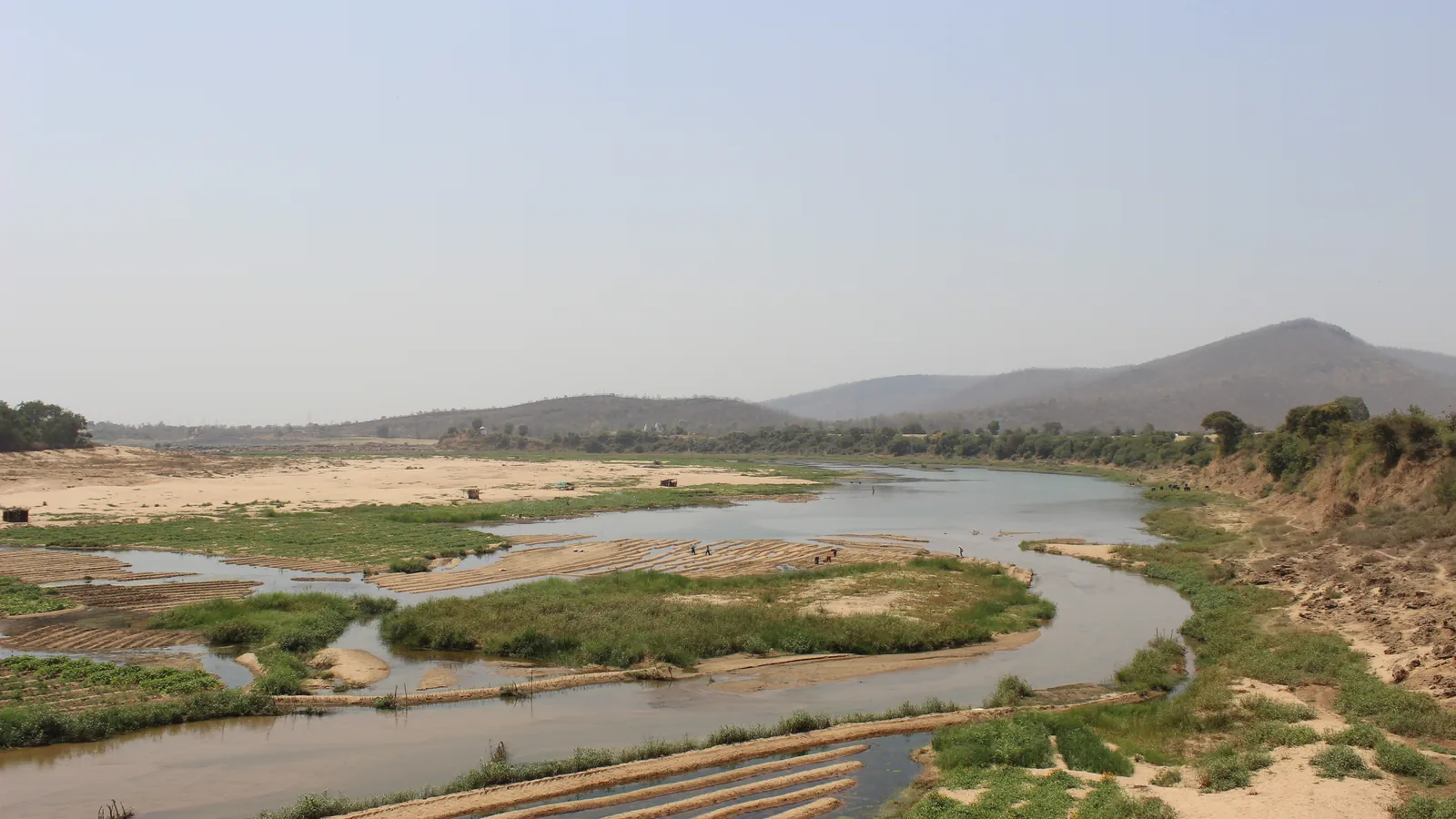 Wide river valley with sand bars, braided channels and low hills in the distance