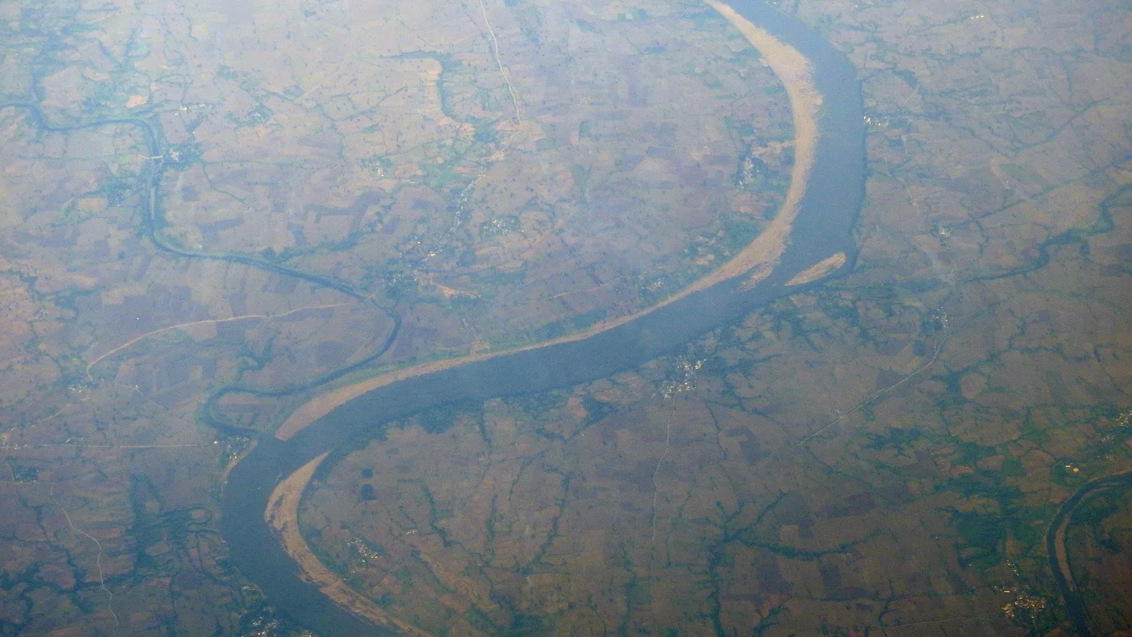 Aerial view of a wide river meandering through cultivated flat land