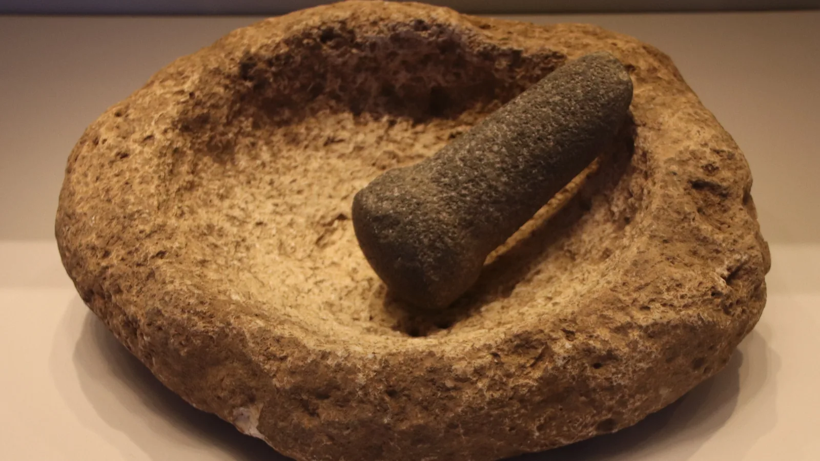 A deep basalt mortar and a limestone mortar with a stone pestle, displayed on a museum stand