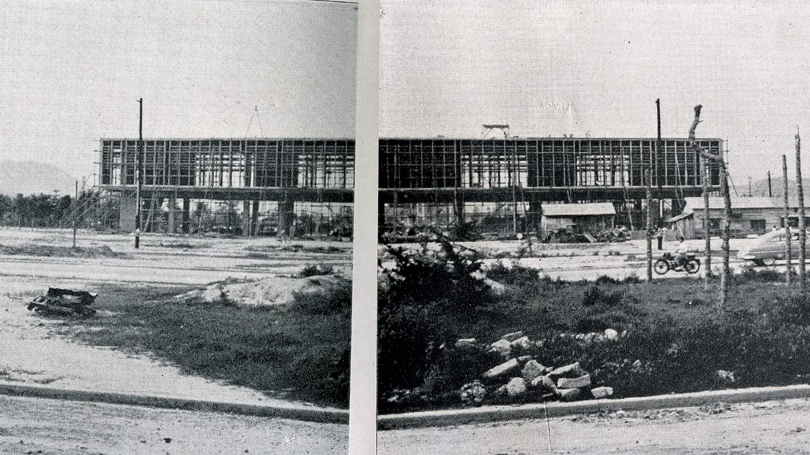 a low modern building on stilts under construction, seen from a distance across an open lot