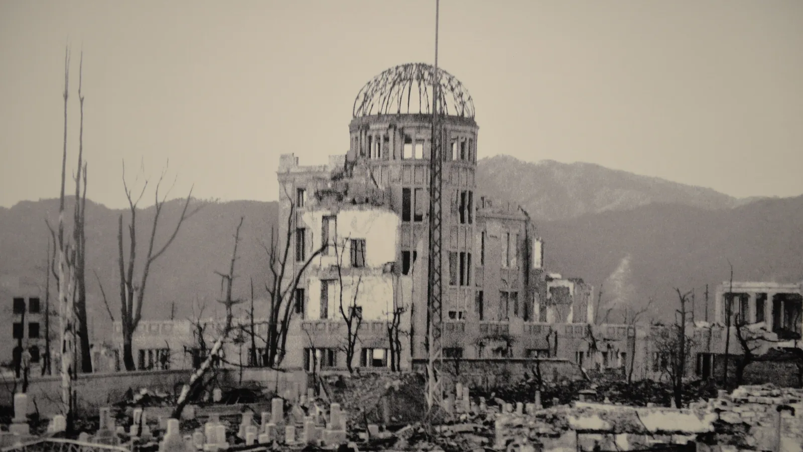 a 1945 photograph of the ruined domed building standing amid rubble and bare trees, mountains behind