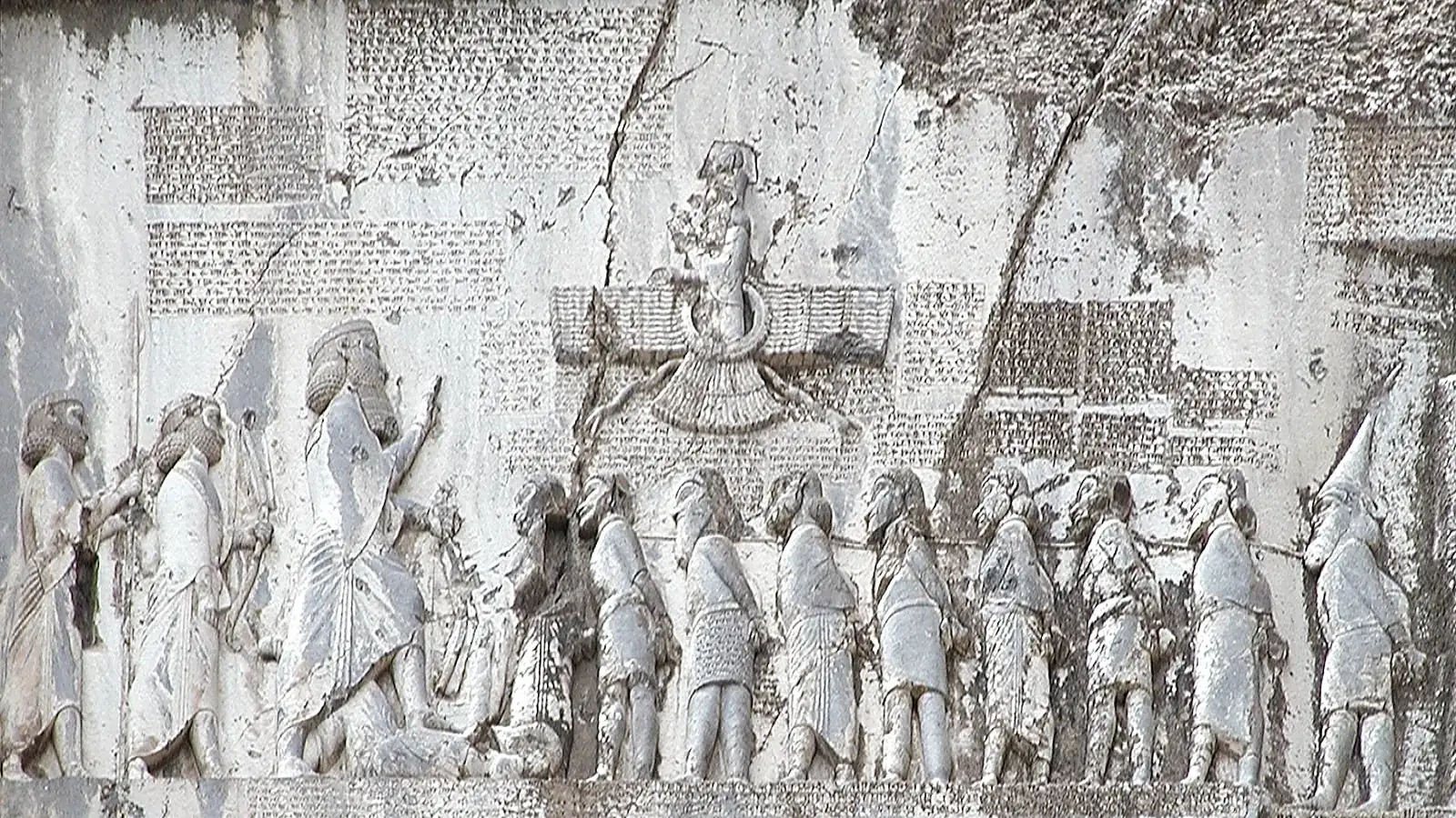 a rock relief showing a king facing a line of bound captives, with cuneiform panels around it