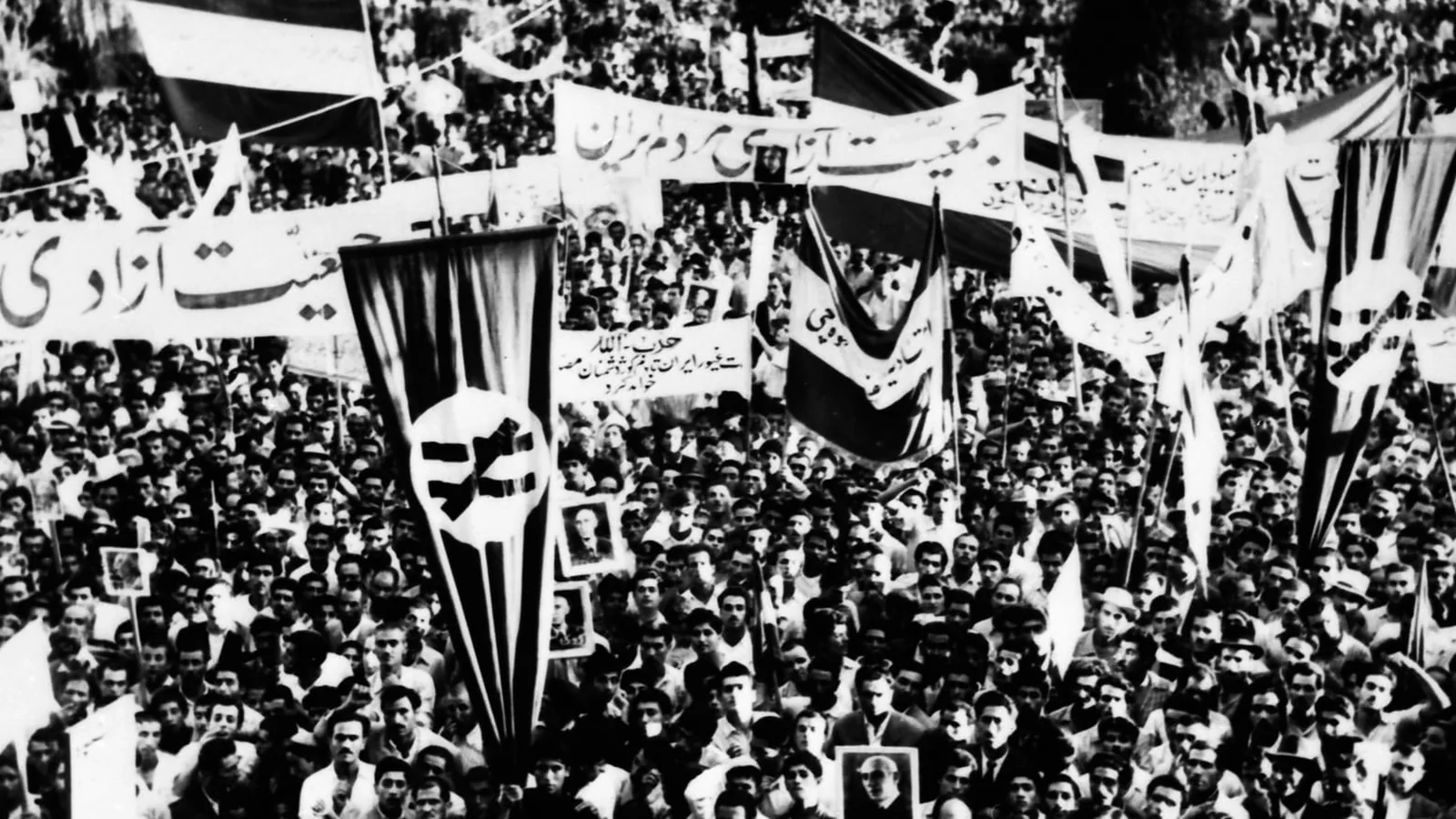 a black and white photograph of a dense crowd filling a square, with banners and placards held up above heads