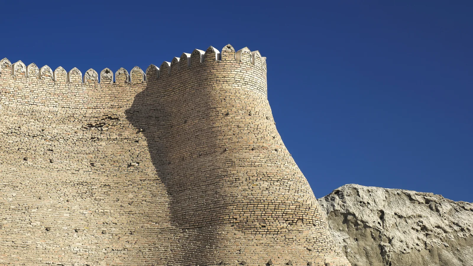 a massive sloped mudbrick fortress wall with towers rising above a city square