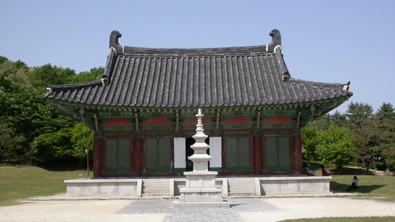 A traditional tiled-roof pavilion and small stone pagoda at a temple site