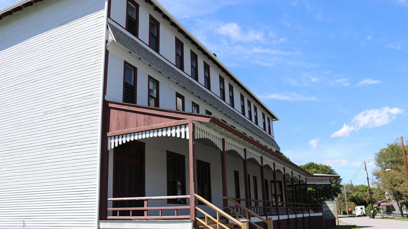 Color photo of a preserved three-story wooden clubhouse with a wraparound porch