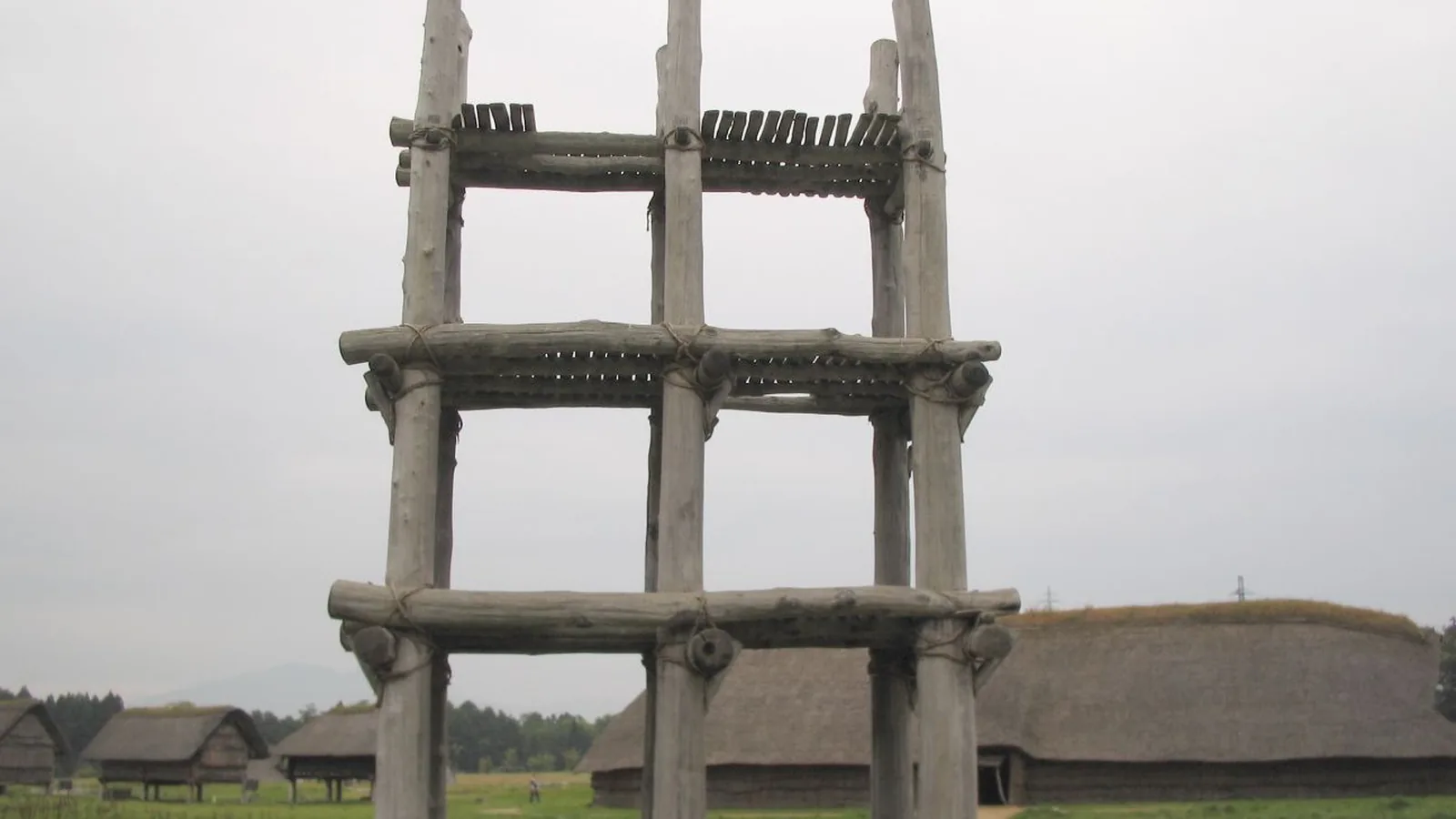 a reconstructed wooden structure of six tall chestnut pillars with platforms, against the sky