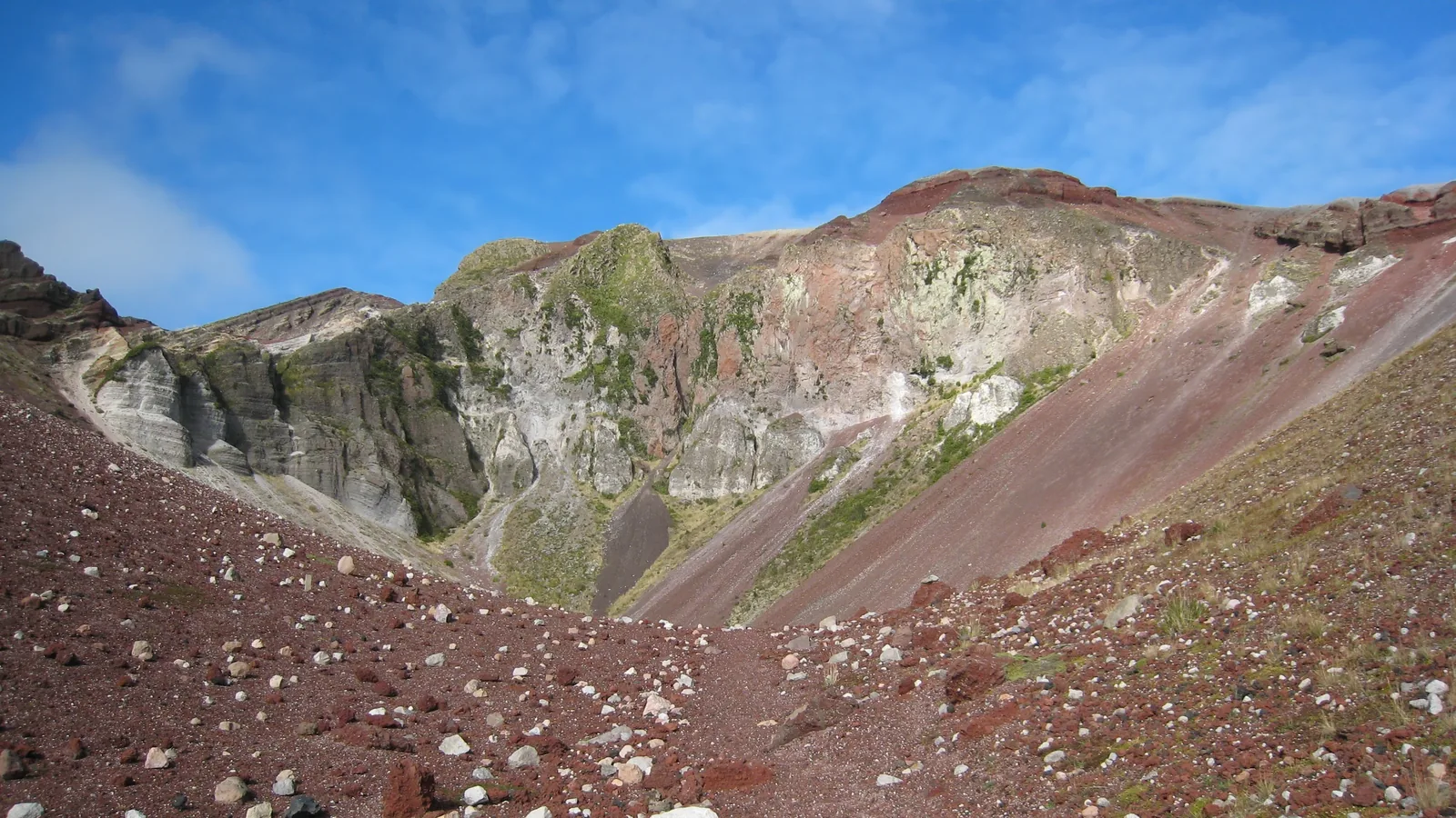 Banded red and white volcanic crater wall inside a mountain rift under blue sky