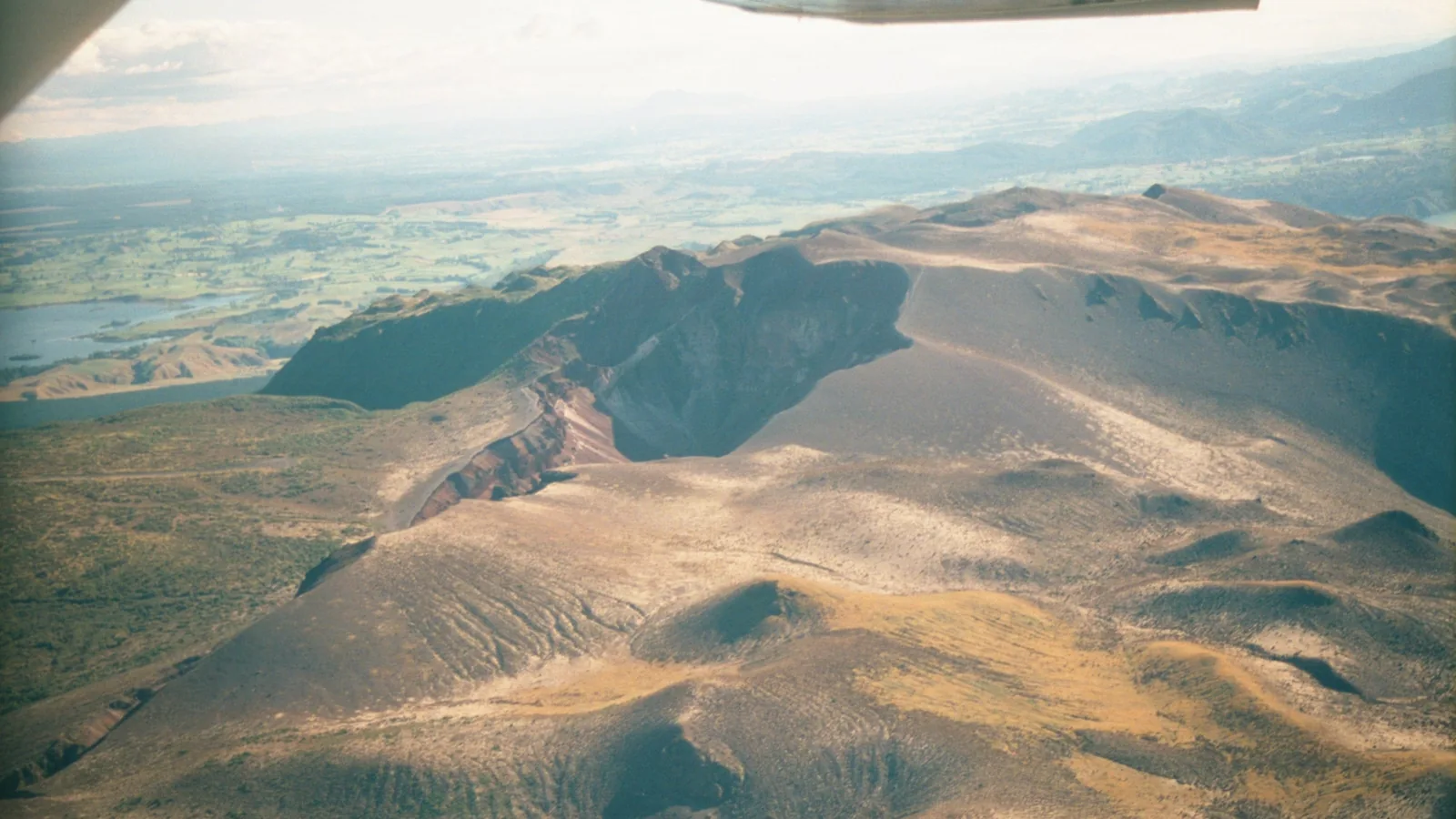 Aerial view of a volcanic crater with a lake visible in the distance