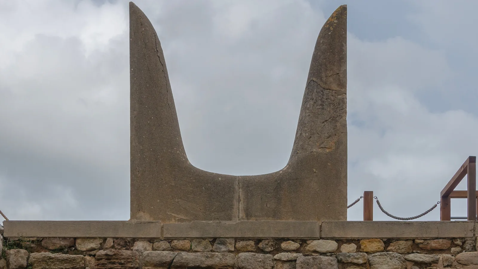 A pair of large pale concrete horns on a wall at Knossos, with hills and sky behind