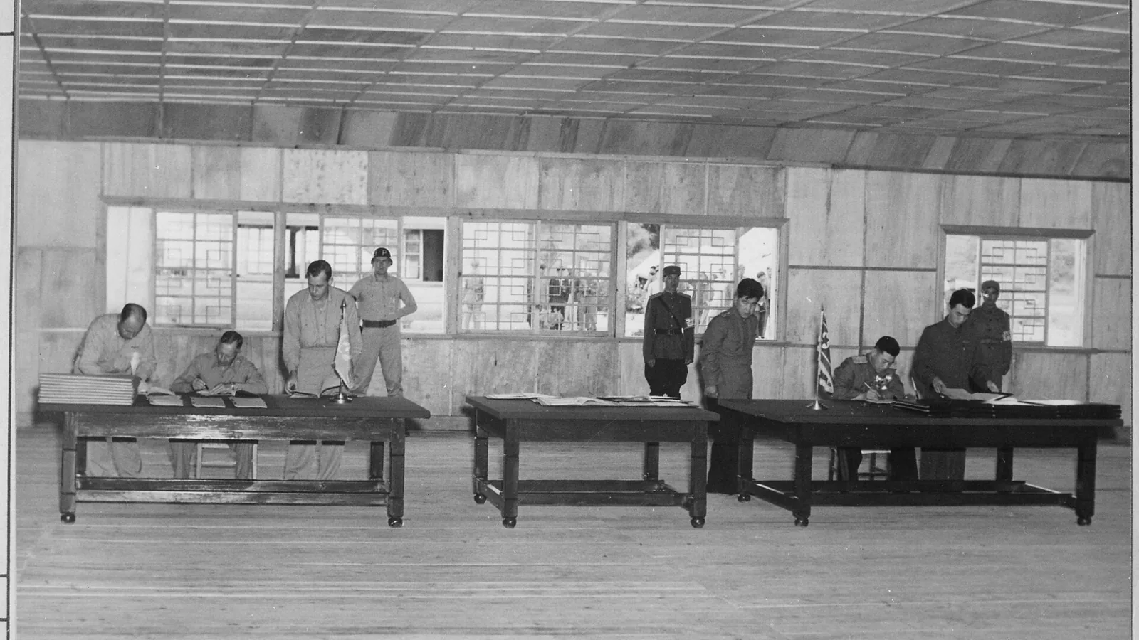 Officers seated at separate tables signing documents in a plain conference hall