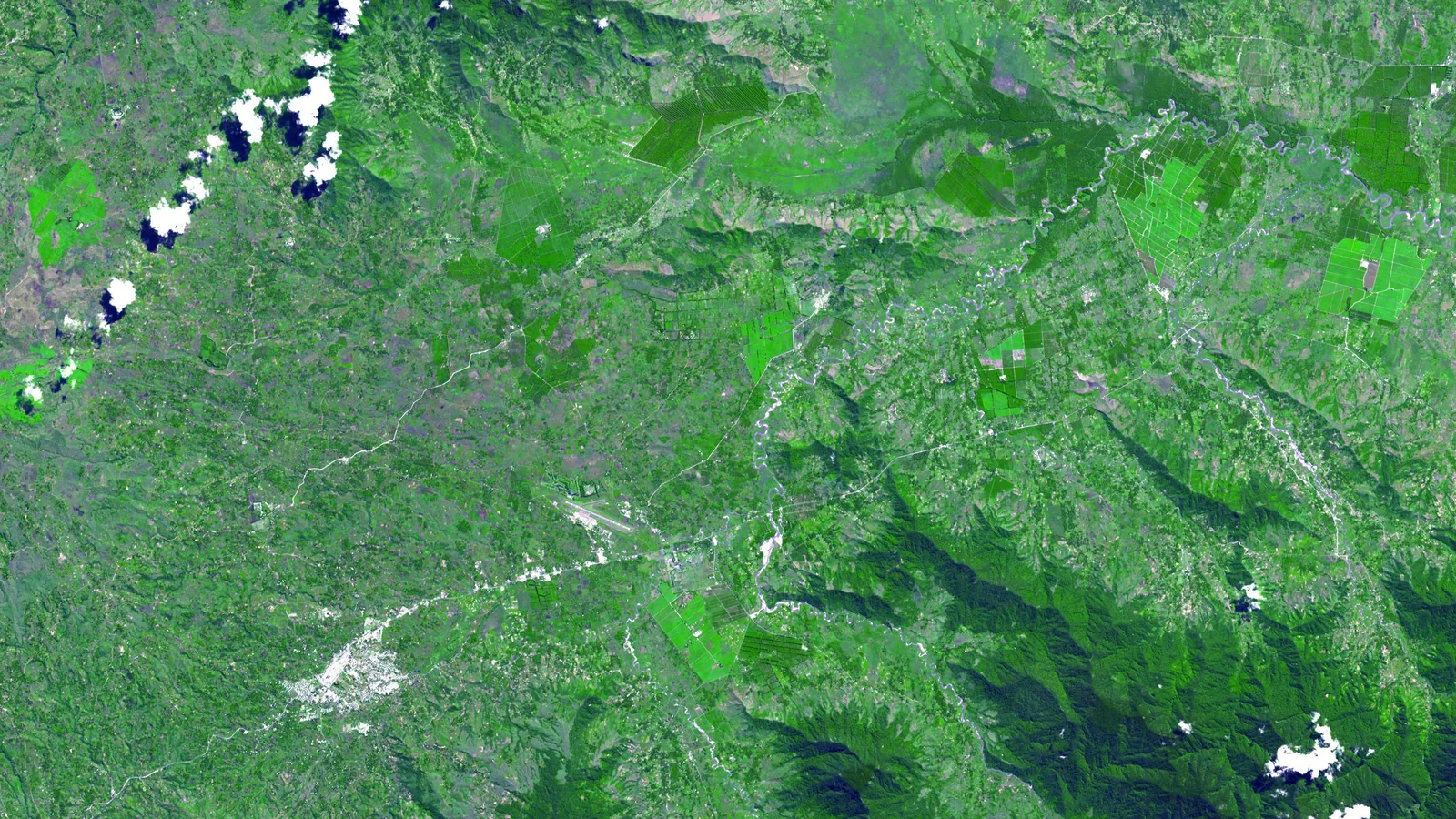 a satellite image of a green mountain valley with pale rectangular fields and small white clouds