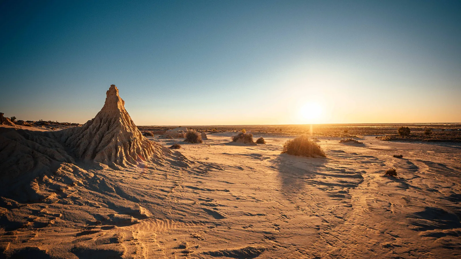 eroded pale clay and sand formations of a dry lake shore at sunset, with a low sun on the horizon