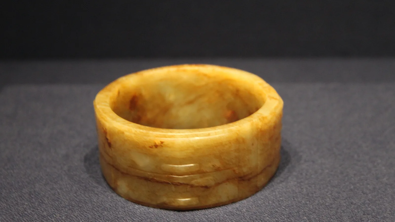 a short yellow-brown jade cong, a square tube with a round bore, lit against a dark grey background