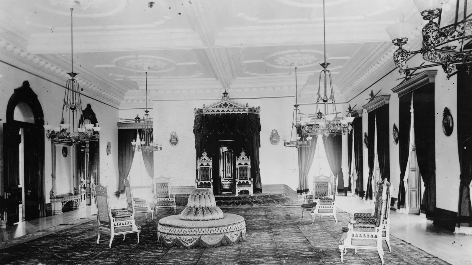 Iolani Palace throne room with red and gold canopy over paired thrones