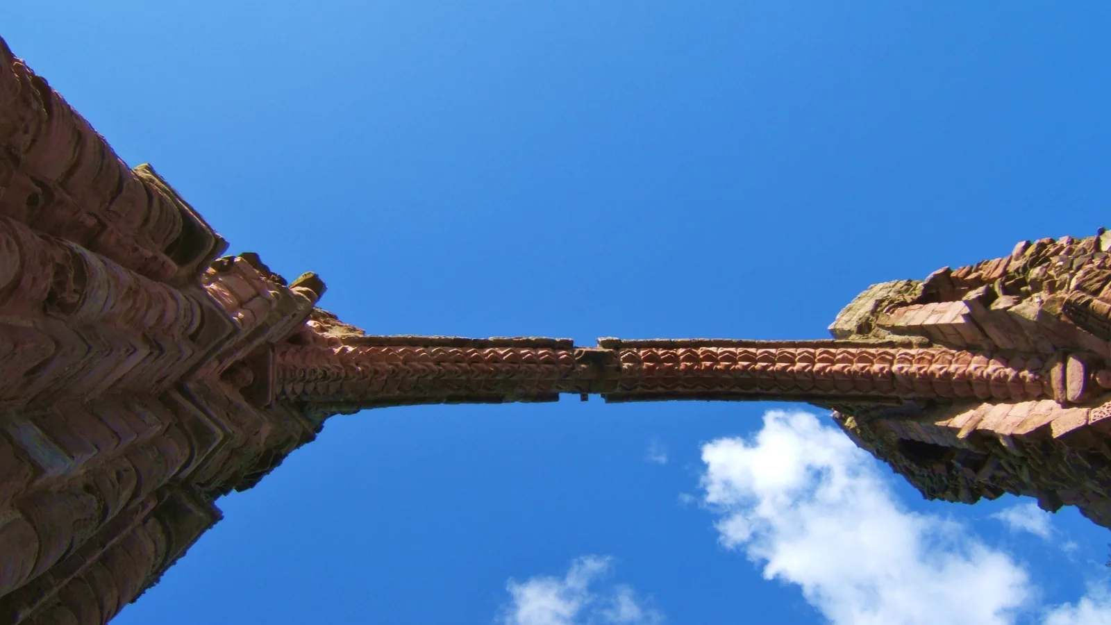Upward view of a surviving stone ribbed arch of Lindisfarne Priory against a blue sky