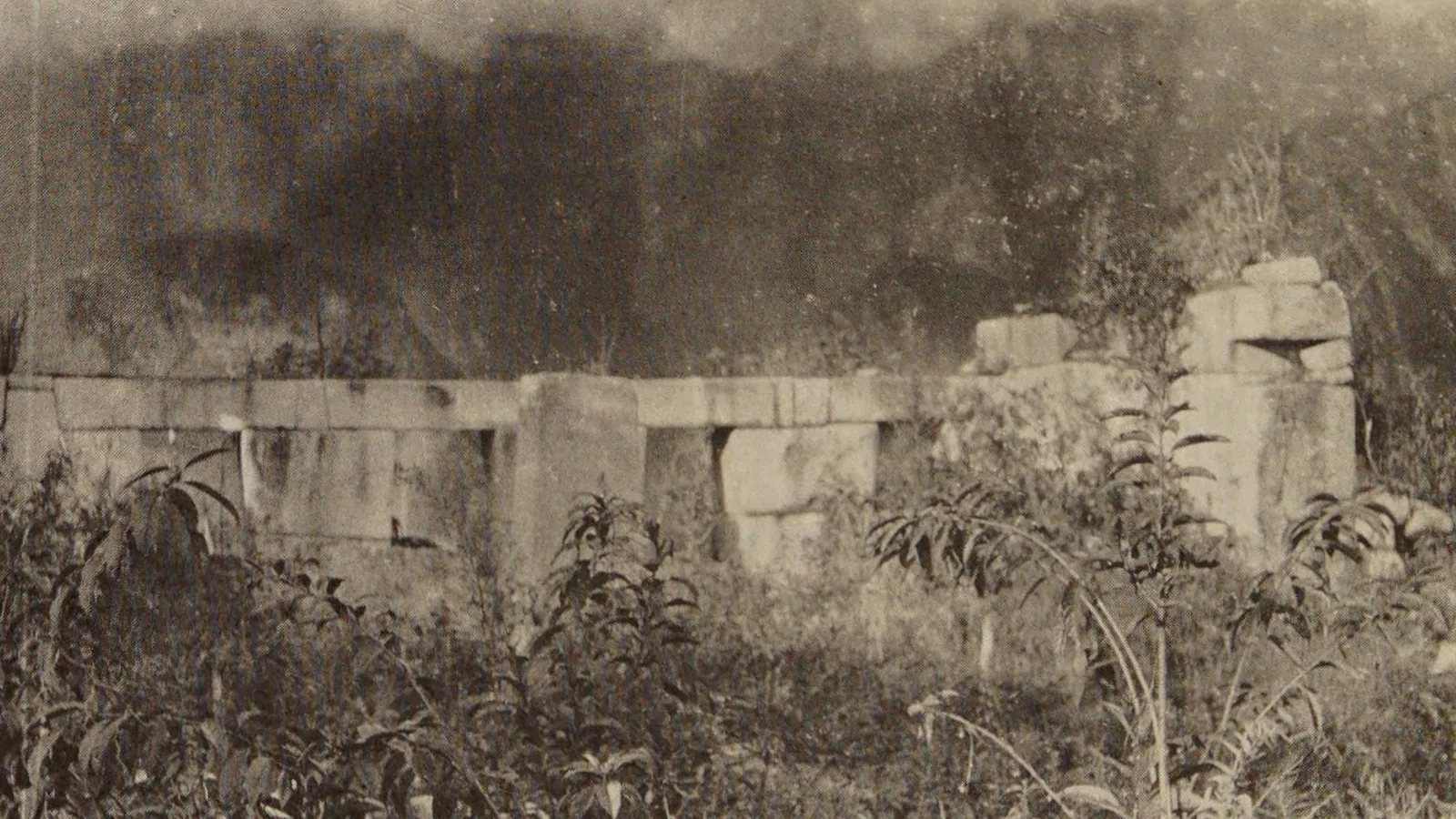 Overgrown stone temple with three window openings facing an open plaza, vegetation covering nearby walls