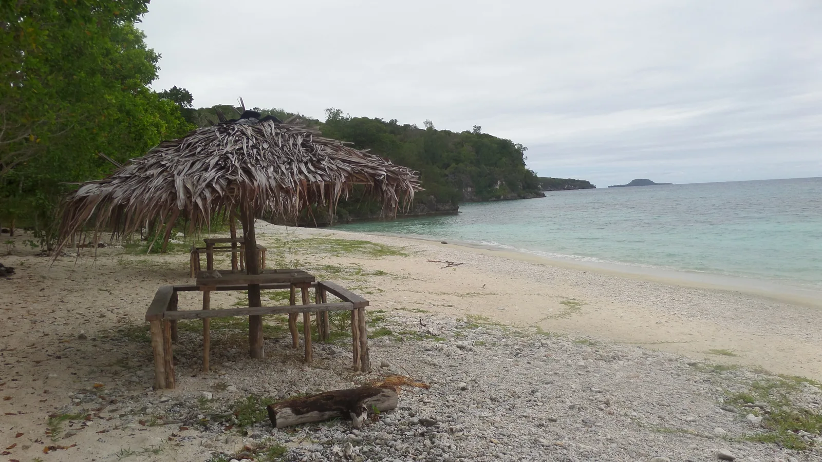 Sandy beach with a thatched shelter, backed by forest and calm turquoise water
