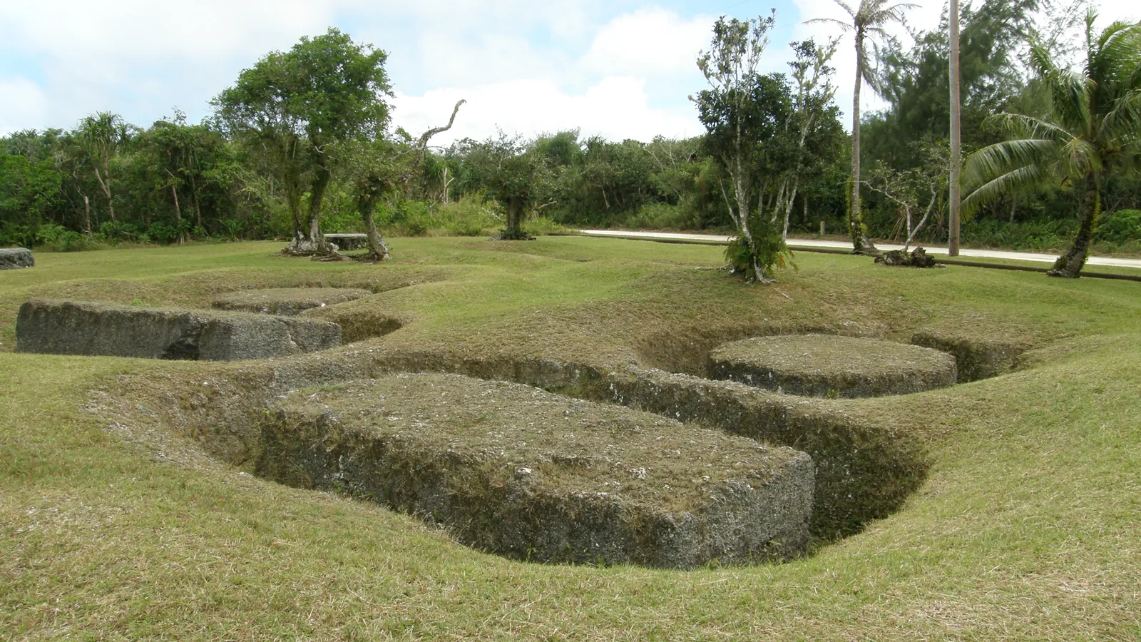 Unfinished latte pillars and round capstones cut into a limestone outcrop among trees